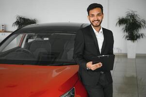 Good looking, cheerful and friendly indian salesman poses in a car salon or showroom. photo