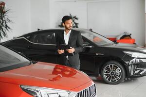 handsome indian salesman presenting new car to clients photo