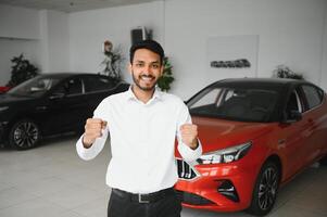 Indian man adult customer male buyer client wears classic suit white shirt chooses auto wants to buy new automobile touch check car in showroom vehicle salon dealership store motor show indoor. photo