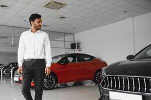 Good looking, cheerful and friendly indian salesman poses in a car salon or showroom. photo