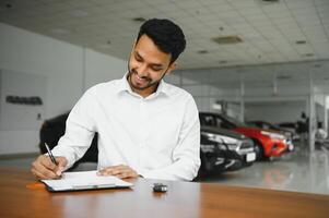 young indian man signing documents at car dealership photo