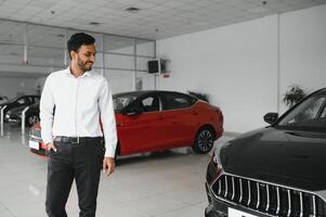 bueno mirando, alegre y simpático indio vendedor poses en un coche salón o sala de exposición. foto