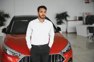 Good looking, cheerful and friendly indian salesman poses in a car salon or showroom. photo