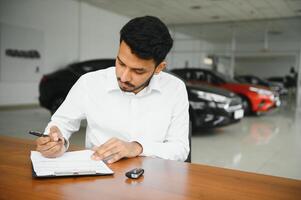 young indian man signing documents at car dealership photo