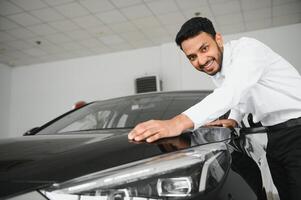 Indian man adult customer male buyer client wears classic suit white shirt chooses auto wants to buy new automobile touch check car in showroom vehicle salon dealership store motor show indoor. photo