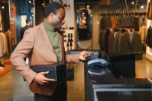 Happy african shopper holding boxes of new clothes or shoes and paying with phone photo