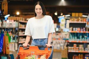 joven sonriente contento mujer 20s en casual ropa compras a supermercado Tienda con tienda de comestibles carro foto