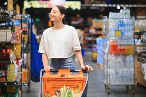 Young smiling happy woman 20s in casual clothes shopping at supermaket store with grocery cart photo