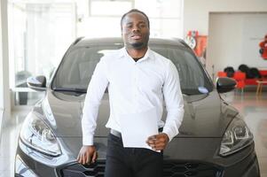 Portrait Of Handsome African American Salesman At Workplace In Car Showroom photo