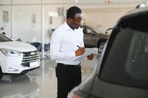 young african american car dealership principal standing in vehicle showroom photo