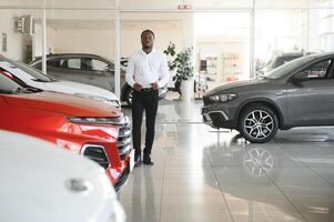 joven africano americano coche concesión principal en pie en vehículo sala de exposición foto