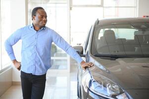 contento coche comprador, nuevo coche propietario concepto. retrato de emocionado joven africano americano chico en concesión sala de exposición foto