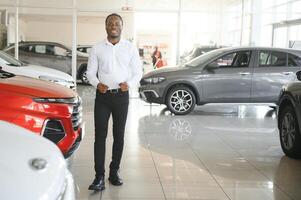 joven africano americano coche concesión principal en pie en vehículo sala de exposición foto