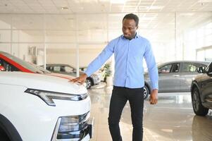 su sueño coche. contento joven africano hombre mirando emocionado elegir un coche a el concesión foto