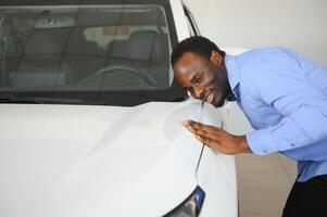 nuevo coche dueño. contento africano americano hombre conmovedor abrazando su Para estrenar auto foto