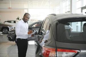 Cars Dealership Concept. Auto Seller Afro Man Standing In Automobile Center photo