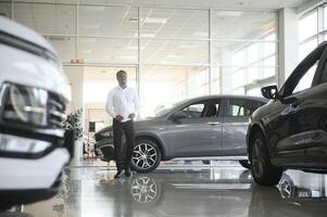 Cars Dealership Concept. Auto Seller Afro Man Standing In Automobile Center photo