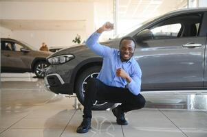 su sueño coche. contento joven africano hombre mirando emocionado elegir un coche a el concesión foto