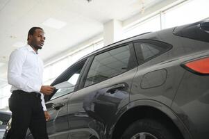 joven africano americano coche concesión principal en pie en vehículo sala de exposición foto