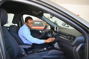Car Owner. Joyful Afro Guy Smiling, Sitting In New Automobile Driving From Dealership Shop photo