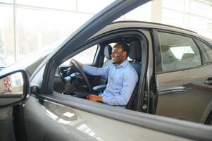 contento coche comprador, nuevo coche propietario concepto. retrato de emocionado joven africano americano chico en concesión sala de exposición foto