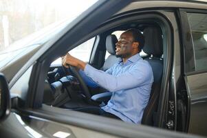 alegre negro hombre sentado en lujo automóvil, prueba conducir, transporte foto