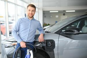 concepto de comprando eléctrico vehículo. hermoso negocio hombre soportes cerca eléctrico coche a concesión foto