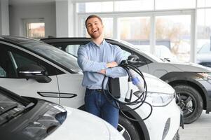 hermoso negocio hombre participación cargando cable para eléctrico coche. caucásico masculino soportes cerca eléctrico auto en concesión foto