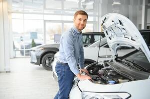 Young man, selling electric cars in the showroom. Concept of buying eco-friendly car for family photo