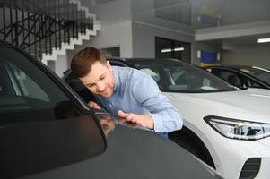 Young man, selling electric cars in the showroom. Concept of buying eco-friendly car for family photo