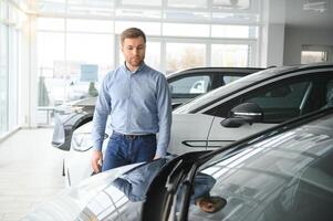 Young man, selling electric cars in the showroom. Concept of buying eco-friendly car for family photo