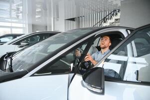 Young man, selling electric cars in the showroom. Concept of buying eco-friendly car for family photo