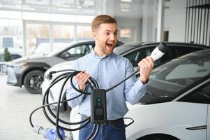 barba hombre molesto un nuevo cargando cable con un coche cargando estación a el motor concesión. concepto de comprando eléctrico vehículo. inteligente ecológico vivo foto