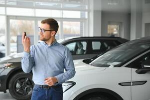 un contento hombre elige un nuevo eléctrico coche a un coche concesión. el concepto de comprando un ecológico coche foto