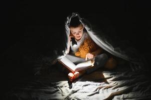 Reading book and using flashlight. Young boy in casual clothes lying down near tent at evening time photo