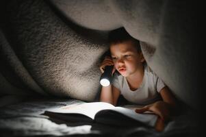 Reading book and using flashlight. Young boy in casual clothes lying down near tent at evening time photo