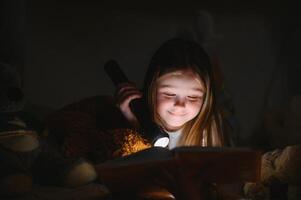 A pretty little girl reading a book on the floor under the lamp. Children and education photo