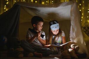 happy family children reading a book with a flashlight in a tent at home. photo