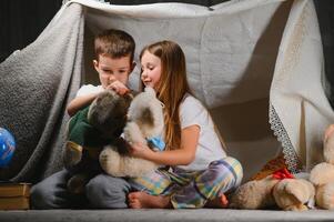 Two little child play at home in the evening to build a camping tent to read books with a flashlight and sleep inside. Concept of game, magic, creativity, alarm systems. photo