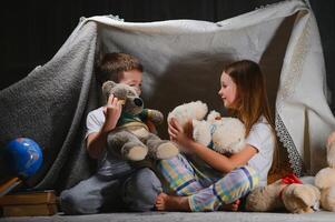 kids lying on floor in cozy nursery. Boy and girl holding flashlights in hands. Children play in a makeshift tent in the nursery photo