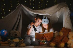 contento familia niños leyendo un libro con un Linterna en un tienda a hogar. foto