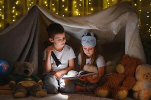 leyendo y familia juegos en para niños carpa. chico y niña con libro y Linterna antes de yendo a cama. foto