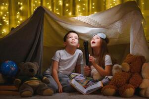 leyendo y familia juegos en para niños carpa. chico y niña con libro y Linterna antes de yendo a cama. foto