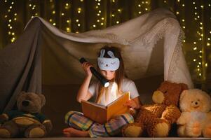 happy child girl laughing and reading book in dark in a tent at home. photo