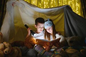 pequeño niños involucrando en leyendo increíble libro. ellos acostado en bonito juguete tienda en cuarto de jugar. chico participación Linterna en mano. foto