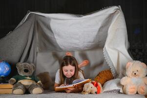 happy child girl laughing and reading book in dark in a tent at home. photo