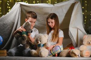 kids lying on floor in cozy nursery. Boy and girl holding flashlights in hands. Children play in a makeshift tent in the nursery photo