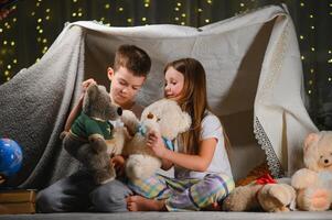 Two little children play at home in the evening to build a camping tent to read books with a flashlight and sleep inside. Concept of game, magic, creativity, alarm systems. photo