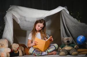 A pretty little girl reading a book on the floor under the lamp. Children and education photo