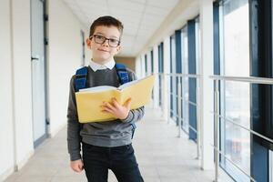 Portrait of happy school student. Smart elementary school kid glasses standing in school. Little child in holding a book photo